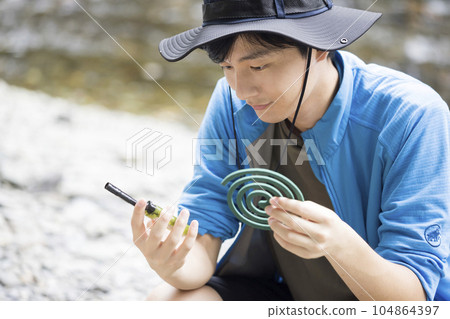 Young man checking the amount of gas remaining in the lighter before lighting a mosquito coil outdoors Outdoor image 104864397