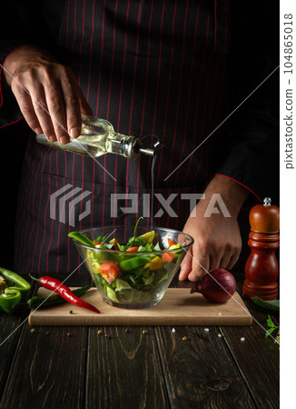 The chef adds fragrant oil to the vegetable salad. Vegetarian food by hands of the cook in the kitchen. The chef adds fragrant oil to the vegetable salad. Vegetarian food by hands of the cook in the kitchen. 104865018