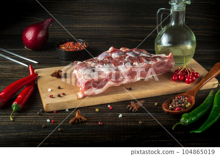 Fresh raw pork ribs on a kitchen cutting board with spices, oil and hot peppers. Cooking delicious food or grilling. 104865019
