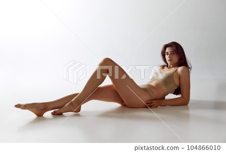 Portrait of attractive young woman with beautiful hair, slim body, lying on floor in underwear against grey studio background 104866010