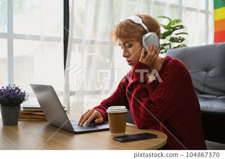 Smiling asian teenage gay man wearing headphone watching movies or studying online on laptop at home 104867370