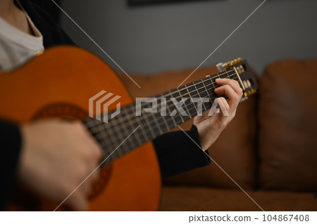Creative hobby, entertainment and leisure concept. Unrecognizable man playing guitar on couch at home Creative hobby, entertainment and leisure concept. Unrecognizable man playing guitar on couch at home 104867408