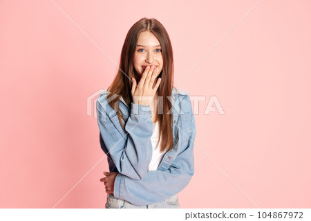 Portrait of young smiling girl covering mouth with hand, feeling surprised against pink studio background Portrait of young smiling girl covering mouth with hand, feeling surprised against pink studio background 104867972