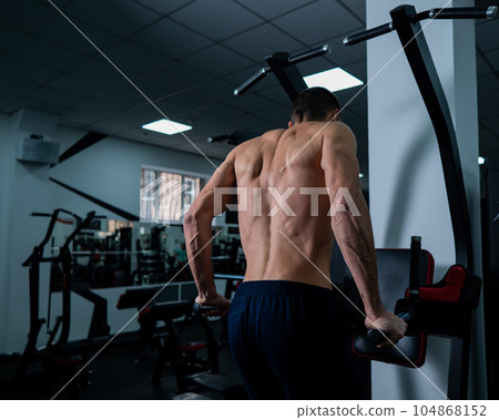 Shirtless man doing triceps dips from parallel bars in gym. Shirtless man doing triceps dips from parallel bars in gym. 104868152