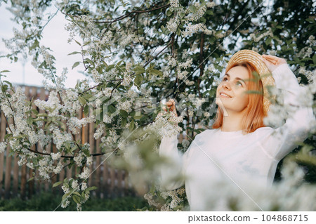 Portrait of a woman in a straw hat in a cherry blossom. Free outdoor recreation, spring blooming garden. Portrait of a woman in a straw hat in a cherry blossom. Free outdoor recreation, spring blooming garden. 104868715