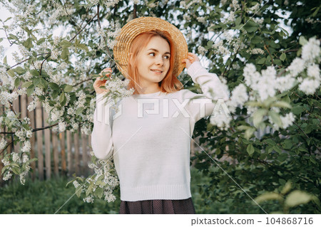 Portrait of a woman in a straw hat in a cherry blossom. Free outdoor recreation, spring blooming garden. 104868716