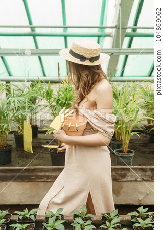 A beautiful young woman takes care of plants in a greenhouse. The concept of gardening and an eco-friendly lifestyle. 104869062
