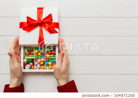 Female hands with delicious candies in box on color background 104871288