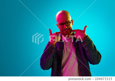 Portrait of young bald man with moustache against blue studio background in neon light. Unpleasant, unhappy face 104871515