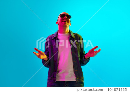 Portrait of stylish young bald man with moustache in sunglasses, laughing against blue studio background in neon light Portrait of stylish young bald man with moustache in sunglasses, laughing against blue studio background in neon light 104871535
