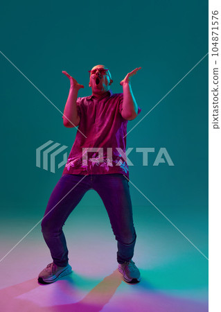 Full-length portrait of emotional young bald man with moustache shouting against cyan studio background in neon light 104871576