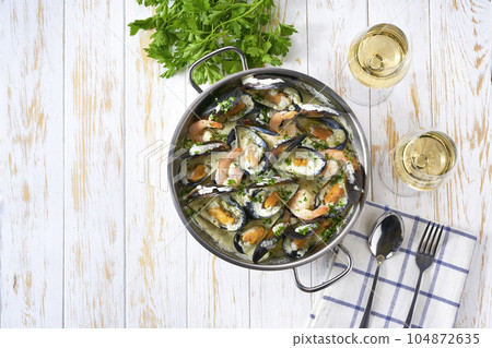 Cream-soup with mussels and white wine on a white wooden table. Cream-soup with mussels and white wine on a white wooden table. 104872635