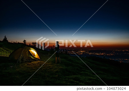 Male tourist stands next to a tourist tent on the summit  104873024