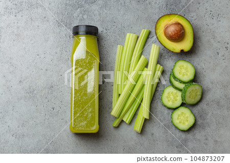 Bottle of green vegetable smoothie with fresh celery sticks, cut avocado, cucumber on gray concrete background top view. Diet beverage, healthy nutrition, detox concept 104873207