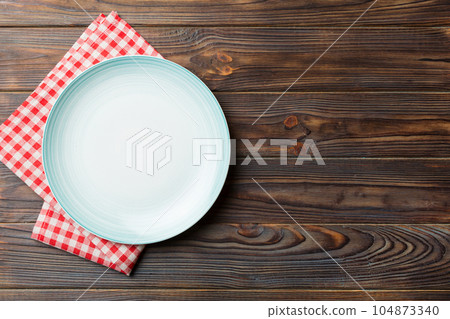 Top view on colored background empty round blue plate on tablecloth for food. Empty dish on napkin with space for your design Top view on colored background empty round blue plate on tablecloth for food. Empty dish on napkin with space for your design 104873340