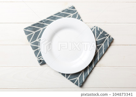 Top view on colored background empty round white plate on tablecloth for food. Empty dish on napkin with space for your design Top view on colored background empty round white plate on tablecloth for food. Empty dish on napkin with space for your design 104873341