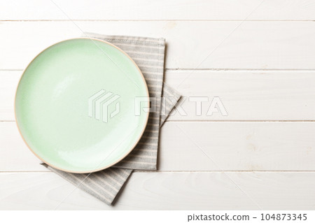 Top view on colored background empty round green plate on tablecloth for food. Empty dish on napkin with space for your design Top view on colored background empty round green plate on tablecloth for food. Empty dish on napkin with space for your design 104873345