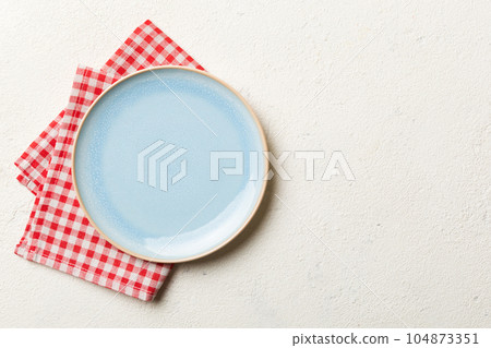 Top view on colored background empty round blue plate on tablecloth for food. Empty dish on napkin with space for your design 104873351