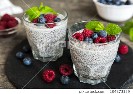 Healthy breakfast or morning with chia seeds vanilla pudding raspberry and blueberry berries on table background, vegetarian food, diet and health concept. Chia pudding with raspberry and blueberry 104873359