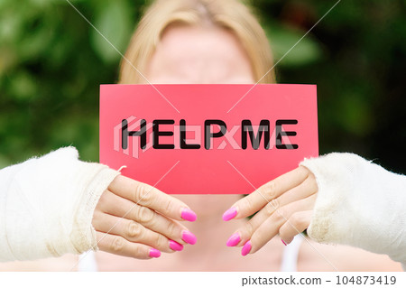 A woman with broken arms in jeans holds a card with the text HELP ME A woman with broken arms in jeans holds a card with the text HELP ME 104873419