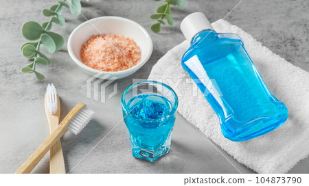 Mouthwash in glass and toothbrush with pink salt on grey table, teeth care Mouthwash in glass and toothbrush with pink salt on grey table, teeth care 104873790