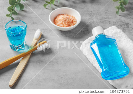 Teeth and gum care with mouthwash and toothbrush with pink salt on grey table background Teeth and gum care with mouthwash and toothbrush with pink salt on grey table background 104873791
