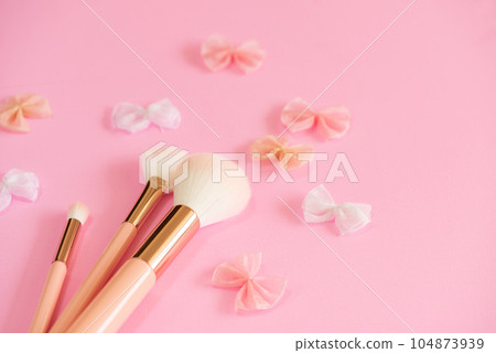 Three makeup brushes and an organza ribbon motif arranged on a pink background Three makeup brushes and an organza ribbon motif arranged on a pink background 104873939