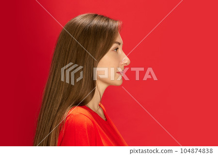 Profile portrait of young beautiful woman looking forward, posing against red studio background 104874838