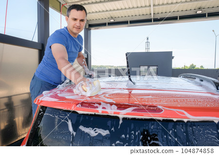 Manual car wash. A man with soapy water washes his car. Cleanliness concept Manual car wash. A man with soapy water washes his car. Cleanliness concept 104874858