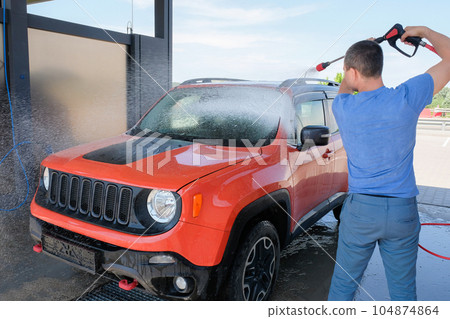 A man washing a car with foam from a hose at a car wash 104874864