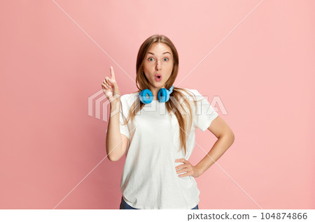 Portrait of young beautiful girl in casual clothes and headphones raising finger up against pink studio background. Ideas Portrait of young beautiful girl in casual clothes and headphones raising finger up against pink studio background. Ideas 104874866