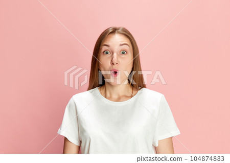 Portrait of beautiful young woman in casual white t-shirt posing with shocked face against pink studio background. Cheerful surprise 104874883