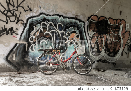 A red bicycle is parked beside the graffiti patterns on the wall. 104875109
