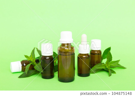 Natural Mint Essential Oil in a Glass Bottle. organic cosmetics with herbal extracts of mint on colored background 104875148