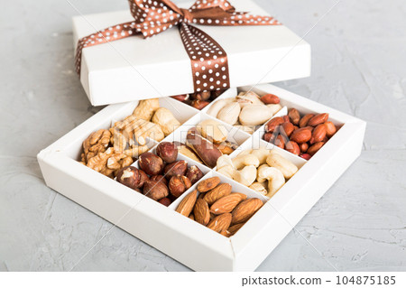 Various varieties of nuts lying in paper box on table background. Top view. Healthy food. Close up, copy space, top view, flat lay. Walnut, pistachios, almonds, hazelnuts and cashews 104875185