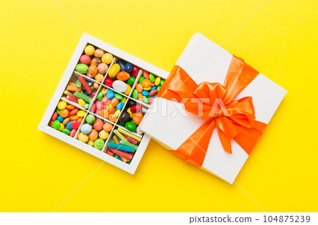 Set of different sweet candy in a paper box with a satin ribbon on a colored background. Holiday concept Set of different sweet candy in a paper box with a satin ribbon on a colored background. Holiday concept 104875239