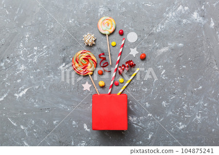 gift box in corner full of assorted traditional candies falling out on colored background with copy space. Happy Holidays sale concept gift box in corner full of assorted traditional candies falling out on colored background with copy space. Happy Holidays sale concept 104875241