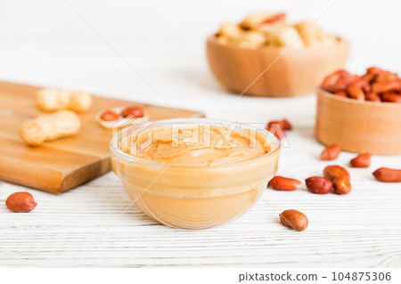 Bowl of peanut butter and peanuts on table background. top view with copy space. Creamy peanut pasta in small bowl Bowl of peanut butter and peanuts on table background. top view with copy space. Creamy peanut pasta in small bowl 104875306