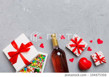 Bottle of red wine on colored background for Valentine Day with gift and chocolate. Heart shaped with gift box of chocolates top view with copy space Bottle of red wine on colored background for Valentine Day with gift and chocolate. Heart shaped with gift box of chocolates top view with copy space 104875308