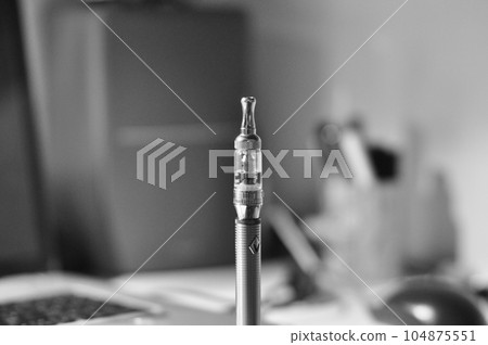 Grayscale closeup of a silver e-cigarette on a table 104875551