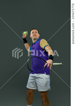 Man, professional tennis player posing with racket, serving ball isolated over grey background 104875778