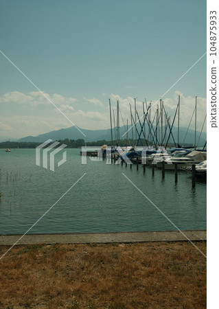 Long row of sailboats by the jetty at the Chiemsee in Breitbrunn am Chiemsee in Bavaria, Germany Long row of sailboats by the jetty at the Chiemsee in Breitbrunn am Chiemsee in Bavaria, Germany 104875933