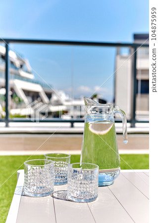 Jug with fresh natural water and empty glasses in terrace 104875959