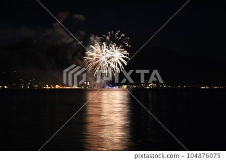 Golden fireworks glowing in the night sky and reflecting on water in Tegernsee, Bavaria, Germany 104876075