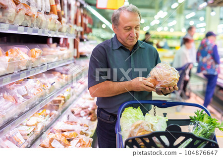 Elderly man chooses chicken meat in supermarket Elderly man chooses chicken meat in supermarket 104876647