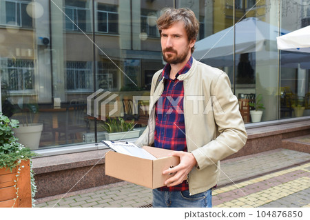 A man with a box of things on the background of an office building. 104876850