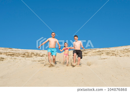 Father and children run to the beach sand on a sunny day. Seed on vacation. Recreation Father and children run to the beach sand on a sunny day. Seed on vacation. Recreation 104876868