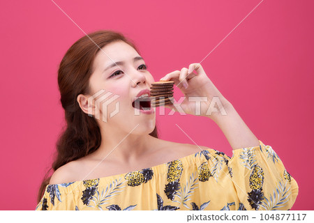 female model wearing a flower-patterned dress with a pink background and enjoying snacks female model wearing a flower-patterned dress with a pink background and enjoying snacks 104877117