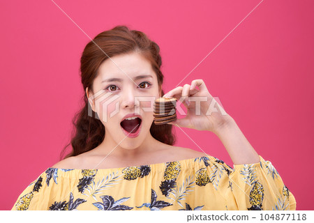 female model wearing a flower-patterned dress with a pink background and enjoying snacks female model wearing a flower-patterned dress with a pink background and enjoying snacks 104877118