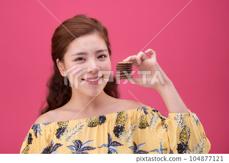 female model wearing a flower-patterned dress with a pink background and enjoying snacks female model wearing a flower-patterned dress with a pink background and enjoying snacks 104877121